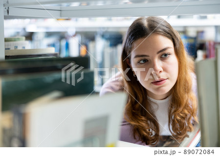 Woman looking for the right book on the bookshelf in public library 89072084