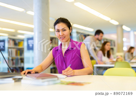 Portrait of positive asian woman with laptop in library 89072169