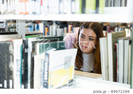 Female student looking for books on shelves in library Female student looking for books on shelves in library 89072266
