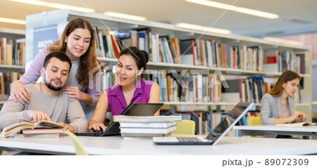 Three adult students work on laptop and read books in a public library 89072309