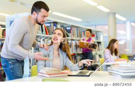 Male librarian helping focused adult student preparing to exam 89072450