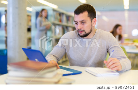 Middle aged man reading books and working on laptop in library 89072451