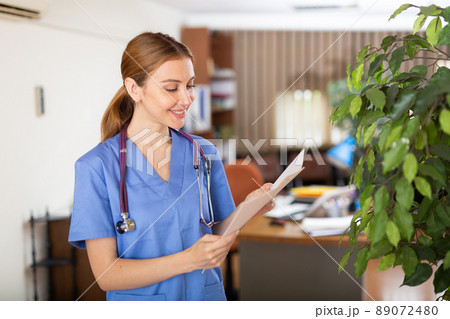 Smiling woman doctor standing in office with papers in hands 89072480