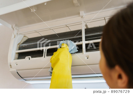 Asian woman cleaning a dirty and dusty air conditioning filter in her house. Housewife removing a dusty air conditioner filter. Asian woman cleaning a dirty and dusty air conditioning filter in her house. Housewife removing a dusty air conditioner filter. 89076729