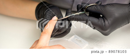 Manicure master removes cuticles from female nails with scissors wearing protective gloves in manicure salon 89078103