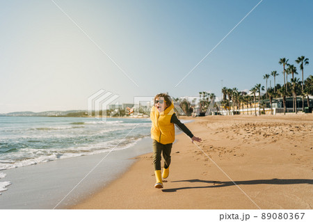 Boy in yellow rubber boots playing with sand at the beach. School kid touching water at autumn winter sea. Child having fun and running. on waves at the shore. Spring Holiday vacation concept Boy in yellow rubber boots playing with sand at the beach. School kid touching water at autumn winter sea. Child having fun and running. on waves at the shore. Spring Holiday vacation concept 89080367