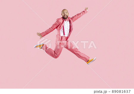 Happy funny young man in suit having fun jumping isolated on pastel pink background. 89081637