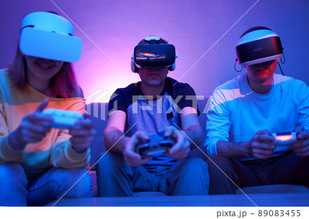Friends playing virtual reality games using joysticks while sitting on the couch. Friends playing virtual reality games using joysticks while sitting on the couch. 89083455
