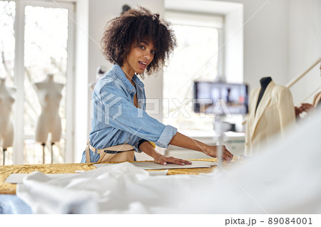 African-American woman draws pattern on fabric sheet shooting video for blog in workshop 89084001