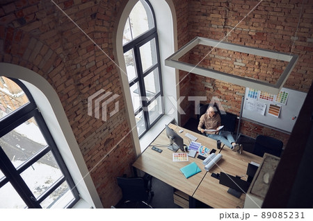 High angle view of creative woman looking at the window while sitting at the table and working on interior design project in modern office 89085231