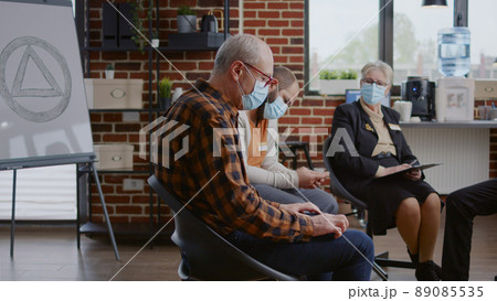 Senior man talking about addiction recovery with people at aa group meeting, receiving advice from therapist during pandemic. Person with face mask having discussion with rehab community Senior man talking about addiction recovery with people at aa group meeting, receiving advice from therapist during pandemic. Person with face mask having discussion with rehab community 89085535