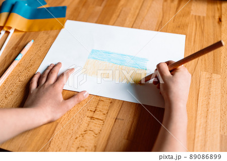 Children hands with yellow and blue color pencil drawing the Ukrainian flag indoor at home 89086899