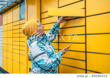Young caucasian woman getting parcel from cell of automatic post terminal outdoors. Young caucasian woman getting parcel from cell of automatic post terminal outdoors. 89086919