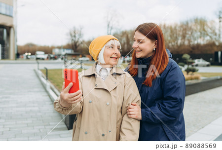 Happy Mother and adult positive daughter are doing Selfie on city street, Urban lifestyle concept. Travelers. Outdoor shot of well-dressed female friends. 89088569