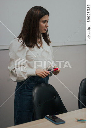 Young female english language teacher with a red marker in a white blouse standing in front of a white board Young female english language teacher with a red marker in a white blouse standing in front of a white board 89093586