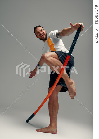 A fighter in white t-shirt and black shorts, stands in a fighting artificially pose and holds a fight stick on studio background. A fighter in white t-shirt and black shorts, stands in a fighting artificially pose and holds a fight stick on studio background. 89095149