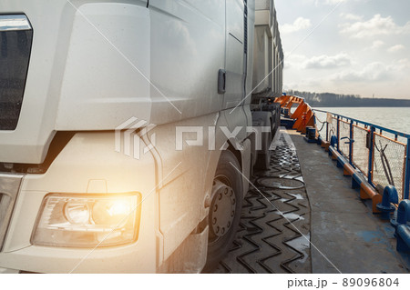 Close-up detail view of big industrial hopper truck body loaded on cargo ferry boat sailing on river or sea port blue sky day background. Freight logistics and comercial shipping transport vessel Close-up detail view of big industrial hopper truck body loaded on cargo ferry boat sailing on river or sea port blue sky day background. Freight logistics and comercial shipping transport vessel 89096804