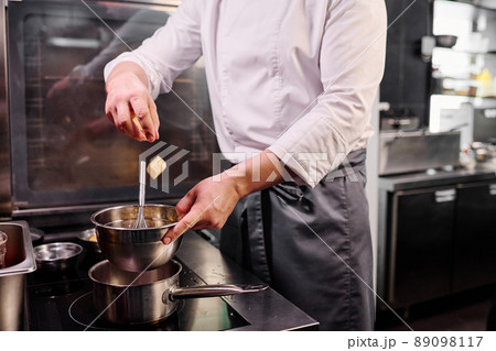 Close-up of chef in apron throwing butter in bowl and melting it on cooker to prepare a dessert Close-up of chef in apron throwing butter in bowl and melting it on cooker to prepare a dessert 89098117