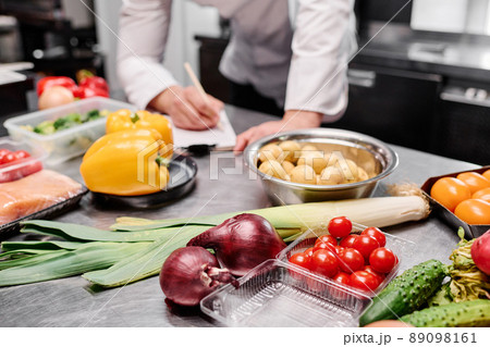 Close-up of fresh vegetables on table in commercial kitchen with chef making menu in background 89098161