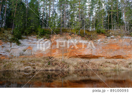 The Echo cliff near river Salaca in Mazsalaca nature park. Beautiful natural formation. A naturally formed cave in the sandstone rock. A river flows along the cave. Devonian period. The Echo cliff near river Salaca in Mazsalaca nature park. Beautiful natural formation. A naturally formed cave in the sandstone rock. A river flows along the cave. Devonian period. 89100093