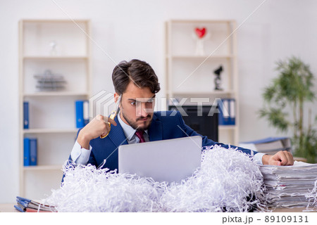 Young male employee and a lot of cut papers in the office 89109131