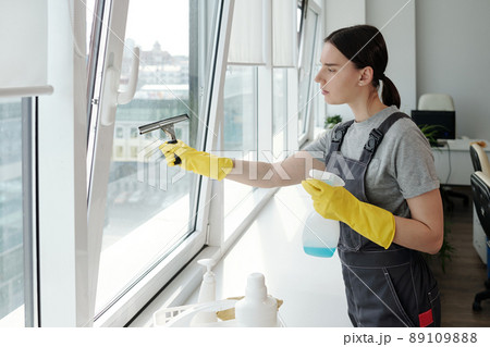 Young female staff of cleaning company washing large window with spatula Young female staff of cleaning company washing large window with spatula 89109888