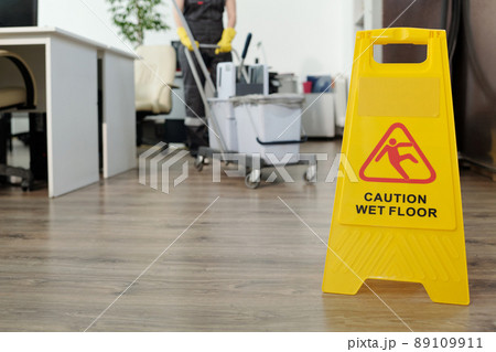 Caution of wet floor on yellow signboard in openspace office against cleaner Caution of wet floor on yellow signboard in openspace office against cleaner 89109911