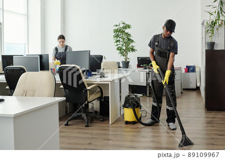 Young African American man in workwear cleaning floor of contemporary office 89109967