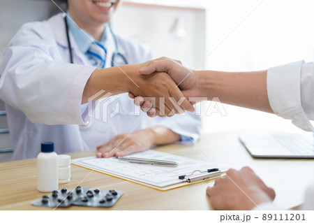 Visiting a doctor concept A male doctor sitting at his desk and checking hand with his patient cheerfully. 89111201