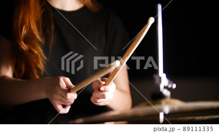 Red-haired girl plays music drums in a dark studio. Hands, drum sticks. 89111335
