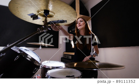 Young red-haired girl working behind a drum set in a dark studio Young red-haired girl working behind a drum set in a dark studio 89111352