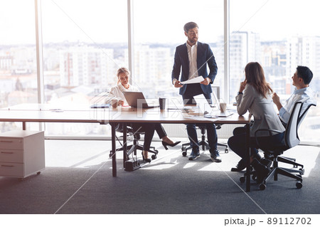 people standing near table, team of young businessmen working and communicating together in office people standing near table, team of young businessmen working and communicating together in office 89112702