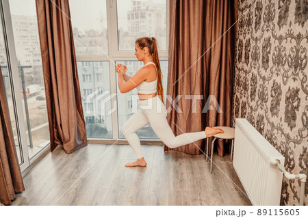 Middle aged athletic attractive woman practicing yoga. Works out at home or in a yoga studio, sportswear, white pants and a full-length top indoors. Healthy lifestyle concept Middle aged athletic attractive woman practicing yoga. Works out at home or in a yoga studio, sportswear, white pants and a full-length top indoors. Healthy lifestyle concept 89115605