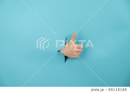A woman's hand sticking out of a hole from a blue background shows a thumbs up. A woman's hand sticking out of a hole from a blue background shows a thumbs up. 89118188