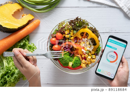 Calories counting , diet , food control and weight loss concept. Calorie counter application on smartphone screen at dining table with salad, fruit juice, bread and fresh vegetable. healthy eating 89118684