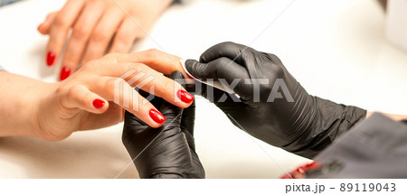 The manicurist finishes the procedure for red nail polishing and cleaning with a cotton napkin, pad, swab in a beauty salon, close up 89119043