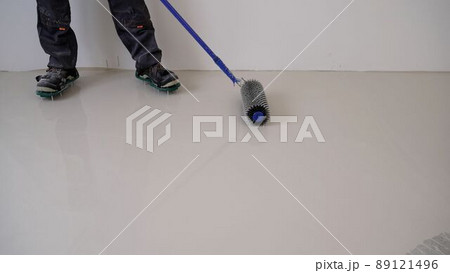 construction worker mixes leveling compound, putties the floor and prepares the floor for parquet laying. A worker levels the floor with a spiked roller. construction worker mixes leveling compound, putties the floor and prepares the floor for parquet laying. A worker levels the floor with a spiked roller. 89121496