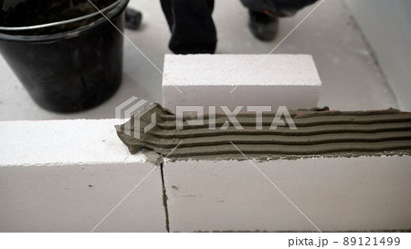 One block is put on another. The builder builds a wall of concrete blocks. Masonry worker make concrete wall by cement block and plaster at construction site. A worker erects a wall of aerated One block is put on another. The builder builds a wall of concrete blocks. Masonry worker make concrete wall by cement block and plaster at construction site. A worker erects a wall of aerated 89121499