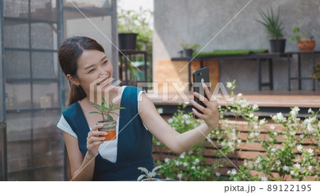 woman taking selfie photo of small tree on pot by smartphone 89122195