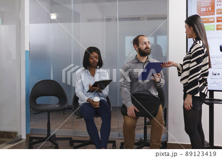 Businesswoman giving cv resume to man applicant asking about work experience during interview meeting in startup company office. Diverse candidates waiting for career opportunity in lobby area 89123419