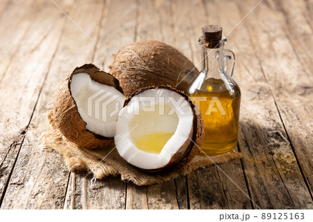 sliced coconuts with oil inside and bottle of coconut oil on wooden table sliced coconuts with oil inside and bottle of coconut oil on wooden table 89125163