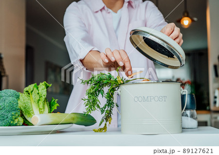 Compost the kitchen waste, recycling at home. Woman putting vegetables cutted leftovers into the garbage, compost bin on the table of kitchen. Environmentally responsible, ecology. Selective focus. 89127621