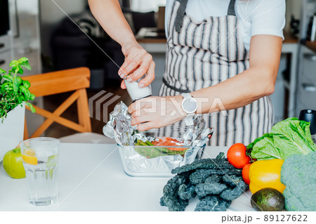 Baked salmon with green asparagus recipe steps. Step three. Woman adding spices and salt to salmon and veggies in the baking form. Step by step recipe. Healthy cooking at home according to recipe 89127622