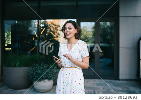 Cheerful woman with smartphone near modern building 89128693