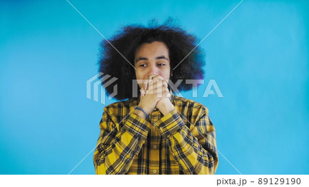 A young man with an African hairstyle on a blue background is happy. Emotions on a colored background. A young man with an African hairstyle on a blue background is happy. Emotions on a colored background. 89129190