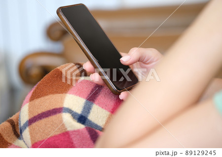 Woman under plaid chatting in social networks using mobile phone closeup 89129245