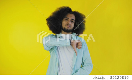 An African-American man looks at the camera, gives a thumbs down, stands isolated on a yellow background 89129816