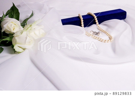 白いバラの花束と青いケースの上の真珠のアクセサリー ドレープの付いた白いベールの背景  白いバラの花束と青いケースの上の真珠のアクセサリー ドレープの付いた白いベールの背景  89129833