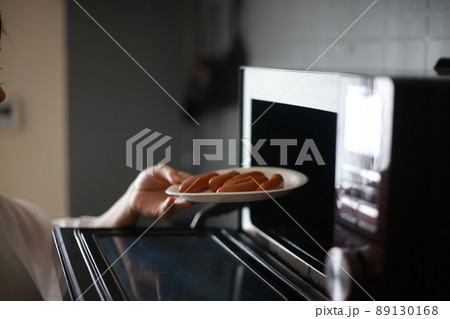 ウインナーを紙皿に並べ電子レンジで温めようとする女性 89130168