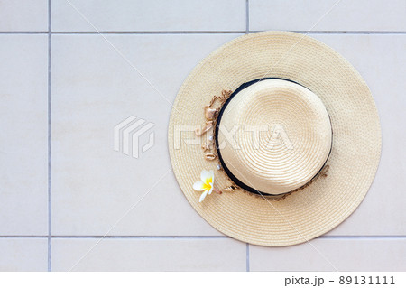 Summer beach straw hat with a necklace with shells and pearls and the plumeria flower on the tiled floor, top view. 89131111